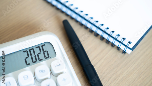 Close-up of calculator displaying 2026 with pen and notebook on wooden desk, representing financial planning, budgeting strategy, and new year preparation concept. © Jokiewalker