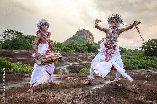 SIGIRIYA, SRI LANKA - DECEMBER 04, 2025 : A Gatabera Player (Getaberakaruwo) and a Ves Dancer or Up Country Dancer perform in front of Sigiriya Rock in Sri Lanka.