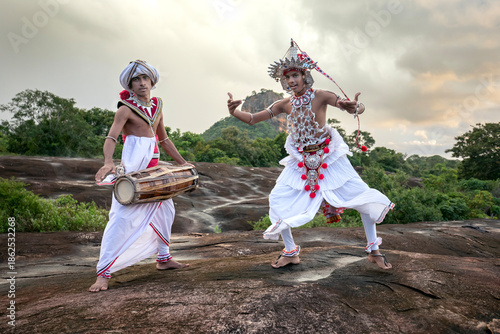 SIGIRIYA, SRI LANKA - DECEMBER 04, 2025 : A Gatabera Player (Getaberakaruwo) and a Ves Dancer or Up Country Dancer perform in front of Sigiriya Rock in Sri Lanka.