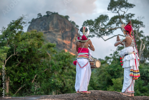 SIGIRIYA, SRI LANKA - DECEMBER 04, 2025 : A Gatabera Player (Getaberakaruwo) and a Ves Dancer or Up Country Dancer perform in front of Sigiriya Rock in Sri Lanka.