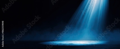 A single beam of blue light shines down onto a dark, smoky stage