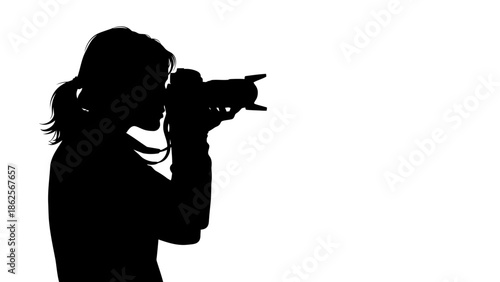 Silhouette of a female photographer holding a professional camera with a large telephoto lens while focusing intently on a distant subject for an image capture