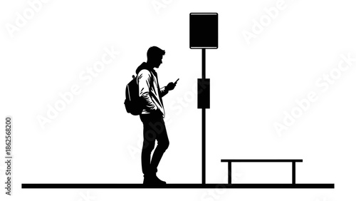 Silhouette of a young male student wearing a backpack standing by a bus stop sign while absorbed in using his modern mobile smartphone technology