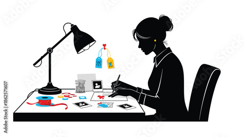 Silhouette of a woman sitting at a desk with a lamp, engaged in crafting and scrapbooking with photos, tags, and ribbons.