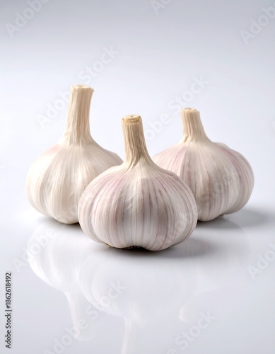 Three whole bulbs of allium sativum, the common kitchen staple, sit on a reflective white surface against a clean backdrop