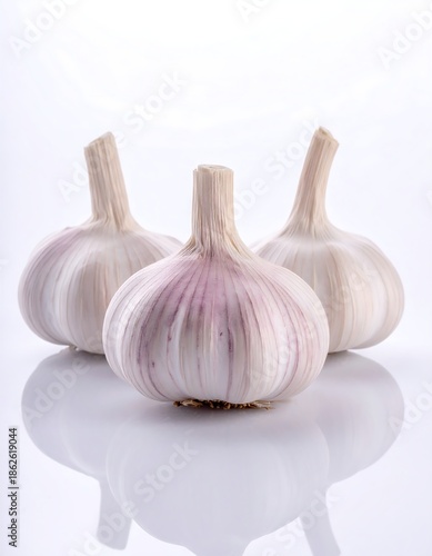 Three whole garlic bulbs, presented on a reflective white surface, with a bright, minimalist aesthetic. The cloves are clustered together