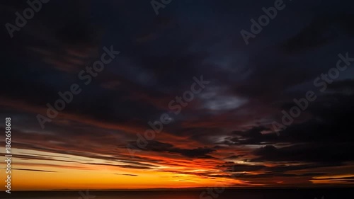 Vibrant sunset over the ocean, with dark clouds streaked with orange and yellow.