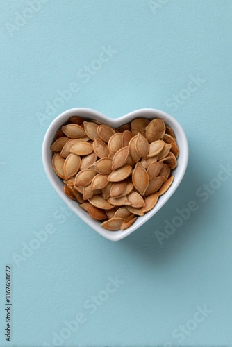 heart shaped bowl of pumpkin seeds on a blue background
