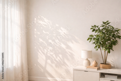 Vászonkép Bright minimalist room with sunlight casting leaf shadows on a white wall and a potted plant on a white cabinet