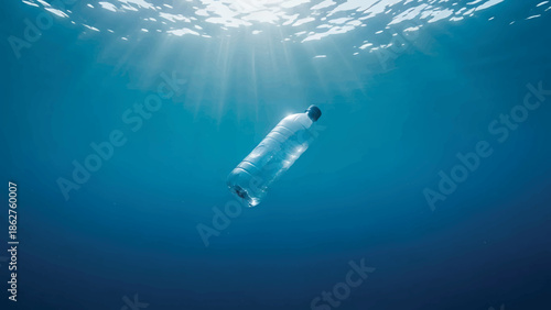 A single plastic bottle drifts in the deep blue ocean, illuminated by sunlight. The bottle is a symbol of pollution