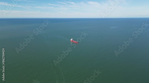 Large cargo ship on emerald sea with red hull. 4K horizontal drone footage shows a big vessel sailing through vivid green water, highlighting its red deck and body in clear daylight.