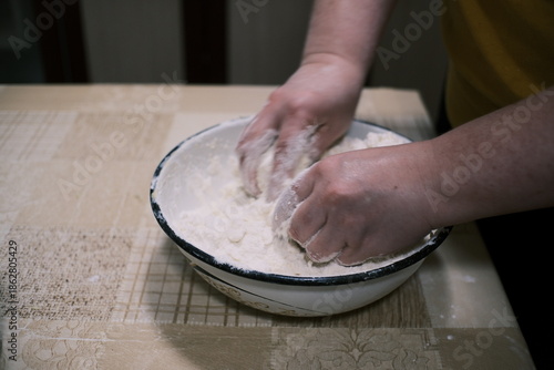 Hands mixing dough in a bowl on a kitchen table, homemade baking process with flour and grated ingredients, close-up food preparation scene showing rustic home cooking and traditional cuisine.