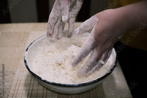 Hands mixing dough in a bowl on a kitchen table, homemade baking process with flour and grated ingredients, close-up food preparation scene showing rustic home cooking and traditional cuisine.