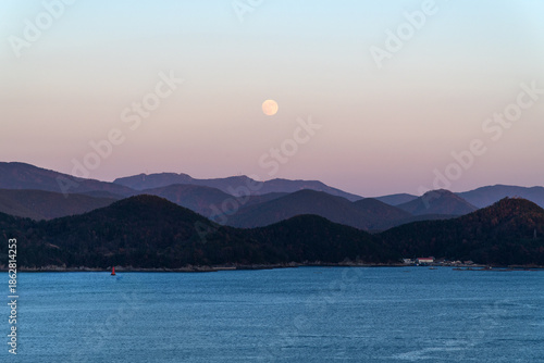 tranquil seascape with a white moon and mountains