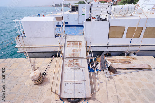 Εκτύπωση καμβά Metal gangway leading to moored boat at dock, nautical ropes and equipment on sunny seaside harbor