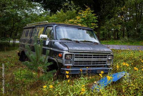 Gray American van abandoned in the woods. The vehicle eaten away by rust and covered in moss.