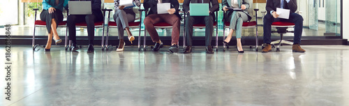 Tableau sur toile Legs of unrecognizable business people group sitting on chairs in a row with resumes and laptops in their hands