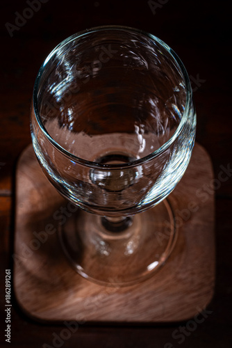 An empty wine glass on a wooden coaster against a dark, dramatic background