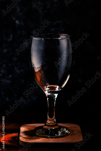A glass of wine on a wooden coaster against a dark, dramatic background