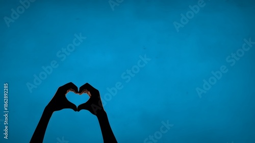 Silhouette of hands forming a heart shape against a blue background. Copy space.