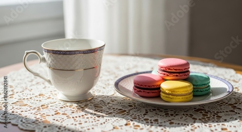 A delicate tea cup and colorful French macarons on a lace tablecloth.