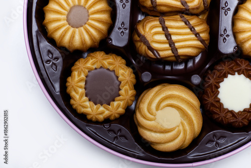 A top-down view of a round tin filled with various types of assorted butter cookies, including chocolate-dipped, swirl, and chocolate-filled varieties. 