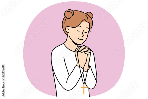 Little girl reads prayer, crossing palms near chest and holding christian cross in hands. Happy pre-teen child praying, feeling involved in catholicism and christian religion at early age