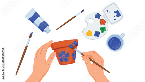 Creative hands meticulously painting delicate blue flowers onto a terracotta pot, surrounded by various art supplies, illustrating a relaxing pottery hobby.