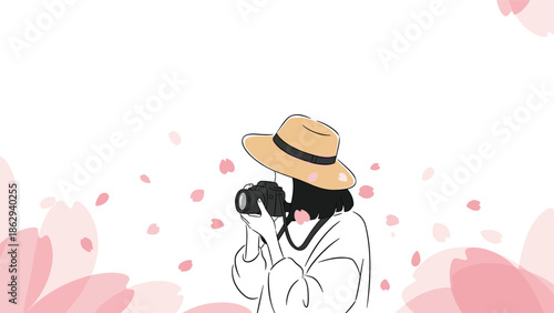 Person wearing a straw hat taking a photograph with a dslr camera among falling pink cherry blossom petals in a spring garden setting.