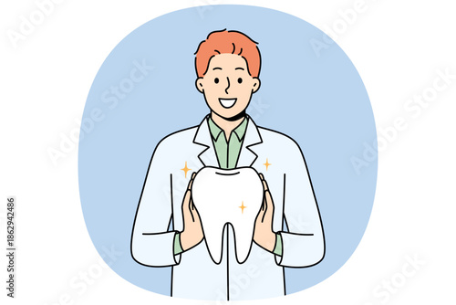 Man orthodontist from dental clinic holds model of healthy tooth, offering you procedure to get rid of caries. Guy orthodontist in white coat smiles, recommending becoming client of new dental center