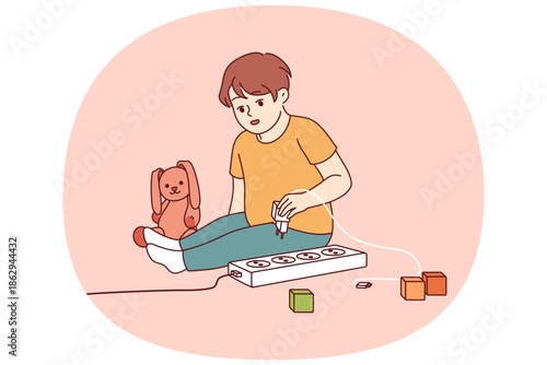 Little boy plays with electrical appliances at risk of getting electric shock due to lack of attention from parents. Child spends time alone playing with electrical outlet that can cause injury