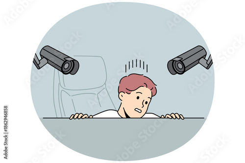 Surveillance cameras above workplace make man feel discomfort and hide from constant monitoring. CCTV system of two cameras in office above workspace, for understanding of big brother