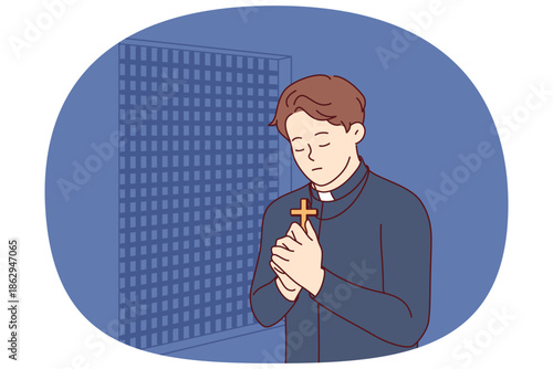 Padre prays and holds christian cross in hands, standing in confession room, asking god to atone for sins of temple visitors. Catholic priest observes ritual of confession and reads prayer