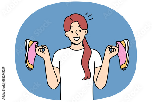 Teenage girl holds running shoes for running or fitness training, recommending use high-quality shoes for sports. Positive woman with beauties in hands invites you to joint workout in gym or marathon