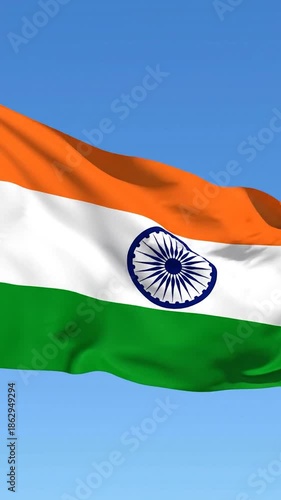 A tricolor flag with a wheel emblem ripples in the wind against a clear blue sky