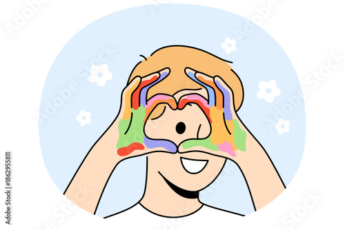 Little artist demonstrates heart gesture with hands, showing love for drawing and using watercolor. Kind boy with palms covered with paints after drawing during lessons in primary school