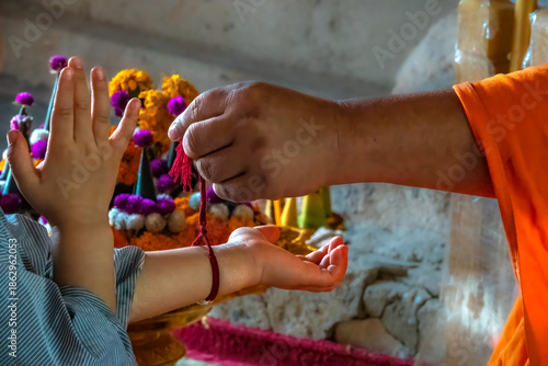 Senior monk attaching a red buddhist bracelet string during a ceremony in Wat Chomphet, on top of a hill across the Mekong River from Luang Prabang, Laos
