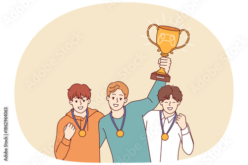 Guys gamers with cup for winning esports tournament celebrate victory and receiving gold medals. Trophy for esports achievement in hands of young men who took first place in cyber competitions