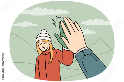 Woman tourist gives five to friend hiking in mountains to explore new picturesque places. Girl in warm jacket and hat enjoys hiking, which allows to improve health and take mind off work.