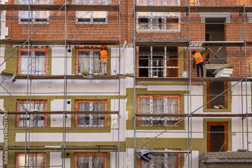 Obraz na płótnie Construction workers in safety gear installing thermal insulation on residential building facade