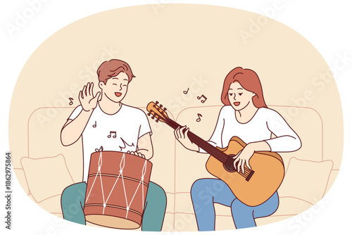 Cheerful friends man and woman playing musical instruments, sitting on sofa and using drum with guitar. Creative guy and girl enjoying playing musical hits during sunday relaxation