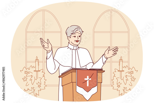 Man priest with smile leads sermon in catholic church, standing behind podium with crucifix, dressed in white robe. Gray-haired priest, rector of temple, encourages visitors to pray get to heaven