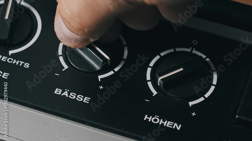 Macro shot of a male hand adjusting bass and treble knobs on a vintage German audio device. The black dials labeled Basse and Hohen are turned to equalize the sound.
