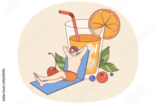 Man relaxed on beach and drinks orange juice from giant glass, enjoying sunny weather. Happy guy sunbathing near pool and enjoy life traveling to resorts with cool hotels for tourists