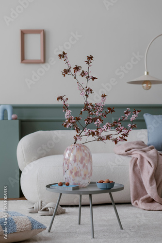 Φωτογραφία Spring composition of living room interior with mock up poster frame, boucle sofa, round coffee table, glass vase with flowering branches, beige carpet and personal accessories