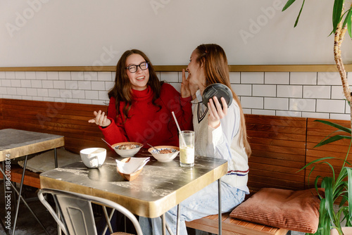 Fotografia Two friends enjoy a joyful conversation while seated at a stylish cafe