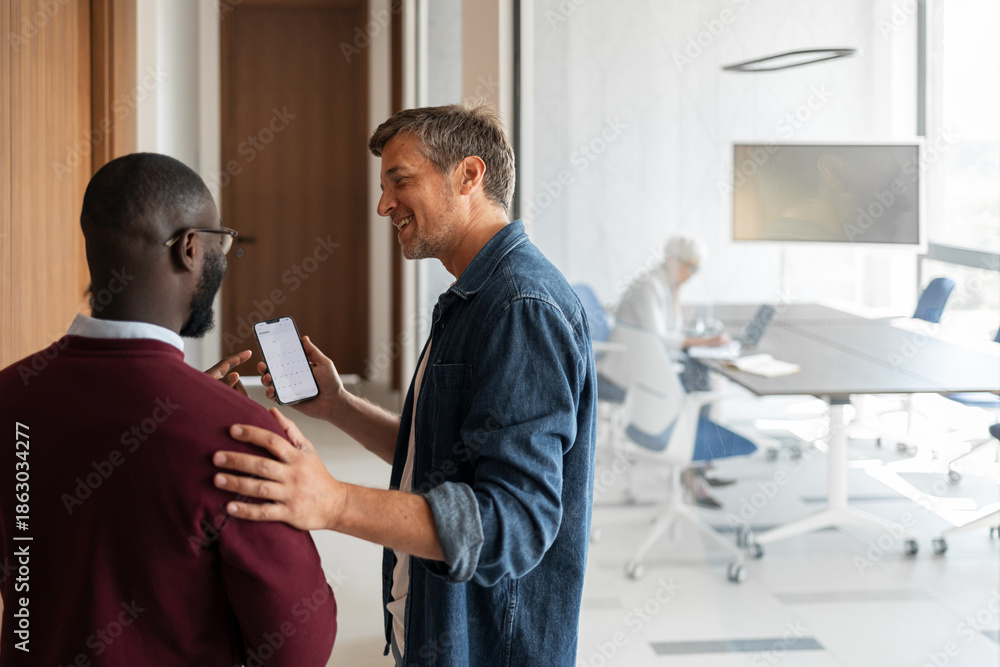 Obraz premium Friendly Colleagues Share a Warm Phone Moment in a Bright Modern Office Workspace