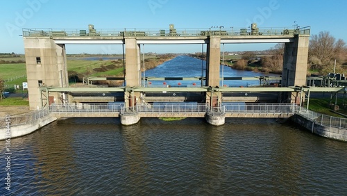 Aerial view of the Denver Sluice, a modern concrete structure reflecting the clear blue sky in the dark water, Downham Market, England, United Kingdom.