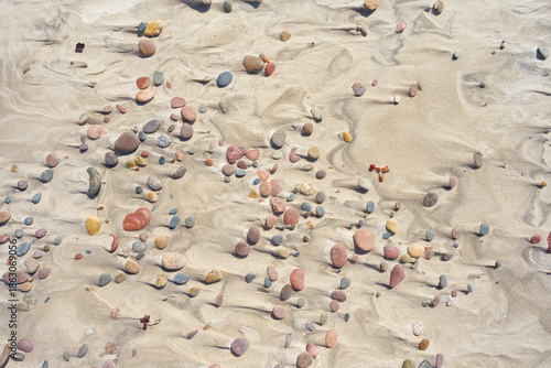 A close-up view of a sandy beach scattered with small, smooth pebbles.