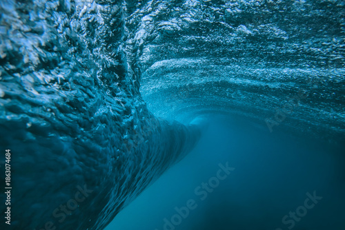 Underwater view breaking ocean wave tunnel deep blue barrel curling above, light filtering through translucent